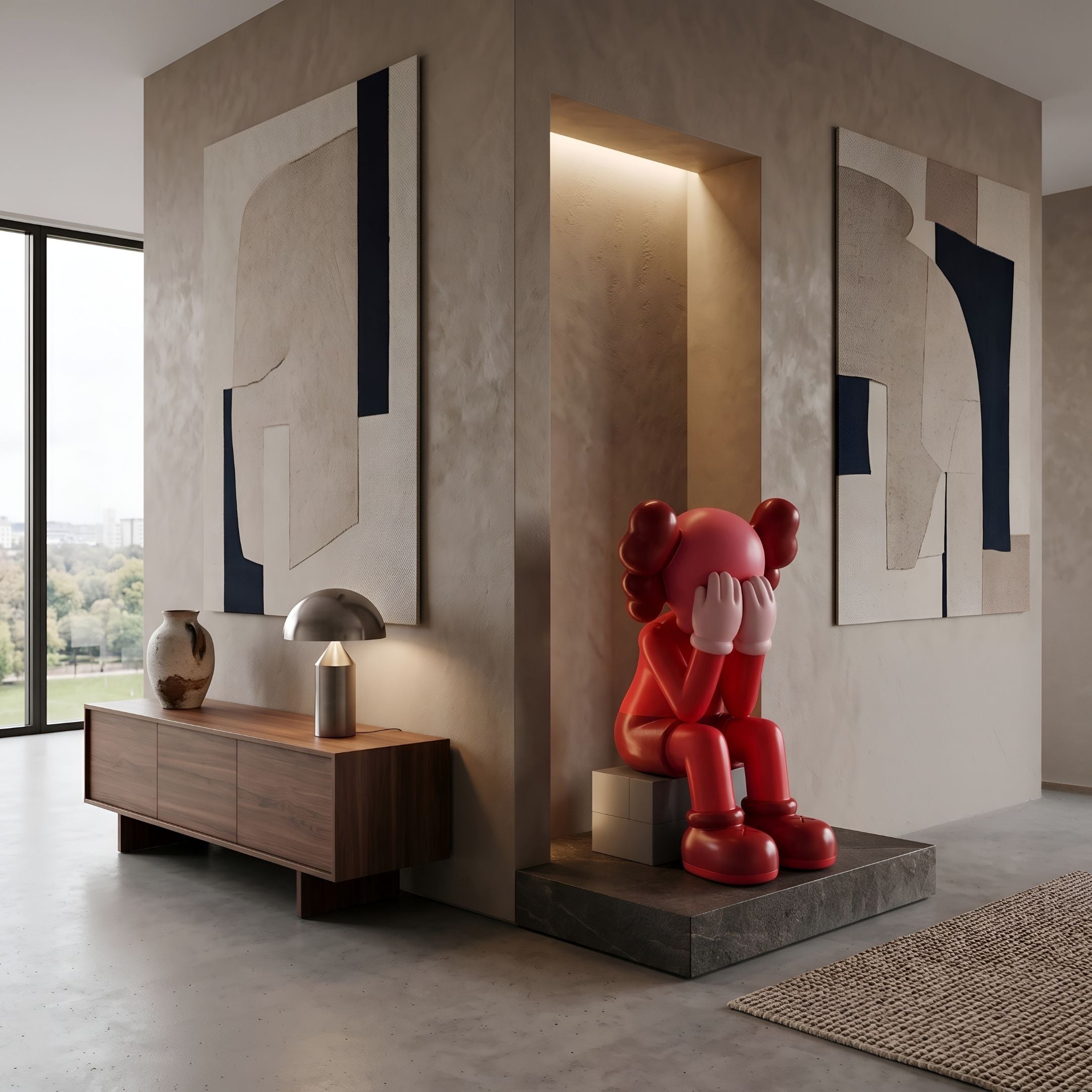 Blush Ruby Iconify Melancholy Sitting Sculpture, 110cm, seated red figure with head in hands on a grey block, displayed on a stone platform in a living room beside a wooden sideboard and abstract wall art.