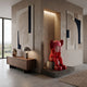 Blush Ruby Iconify Melancholy Sitting Sculpture, 110cm, seated red figure with head in hands on a grey block, displayed on a stone platform in a living room beside a wooden sideboard and abstract wall art.