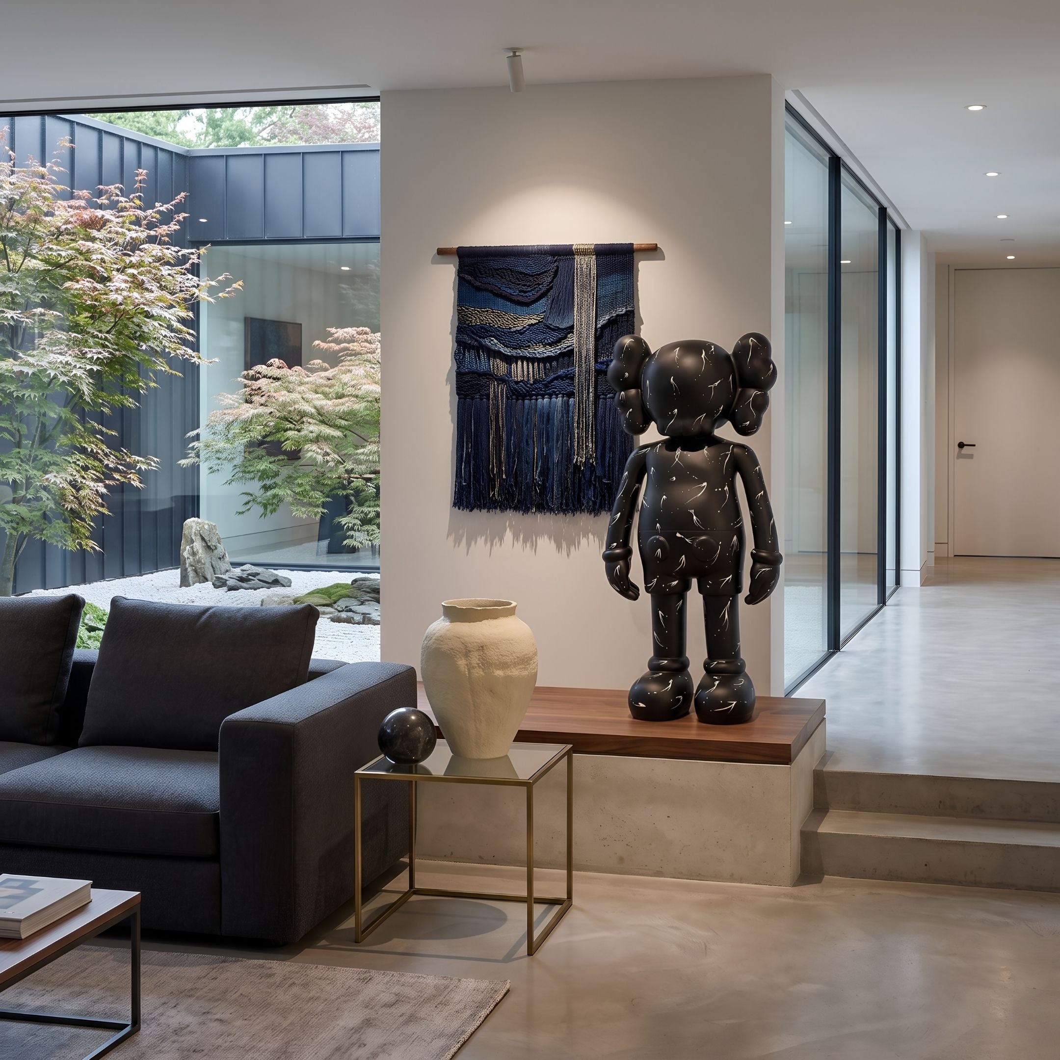 Black Stone Iconify Standing Sculpture, 130cm, in matte black stone-textured resin on a wood-topped platform in a living room beside a dark sofa and wall hanging.