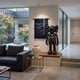 Black Stone Iconify Standing Sculpture, 130cm, in matte black stone-textured resin on a wood-topped platform in a living room beside a dark sofa and wall hanging.
