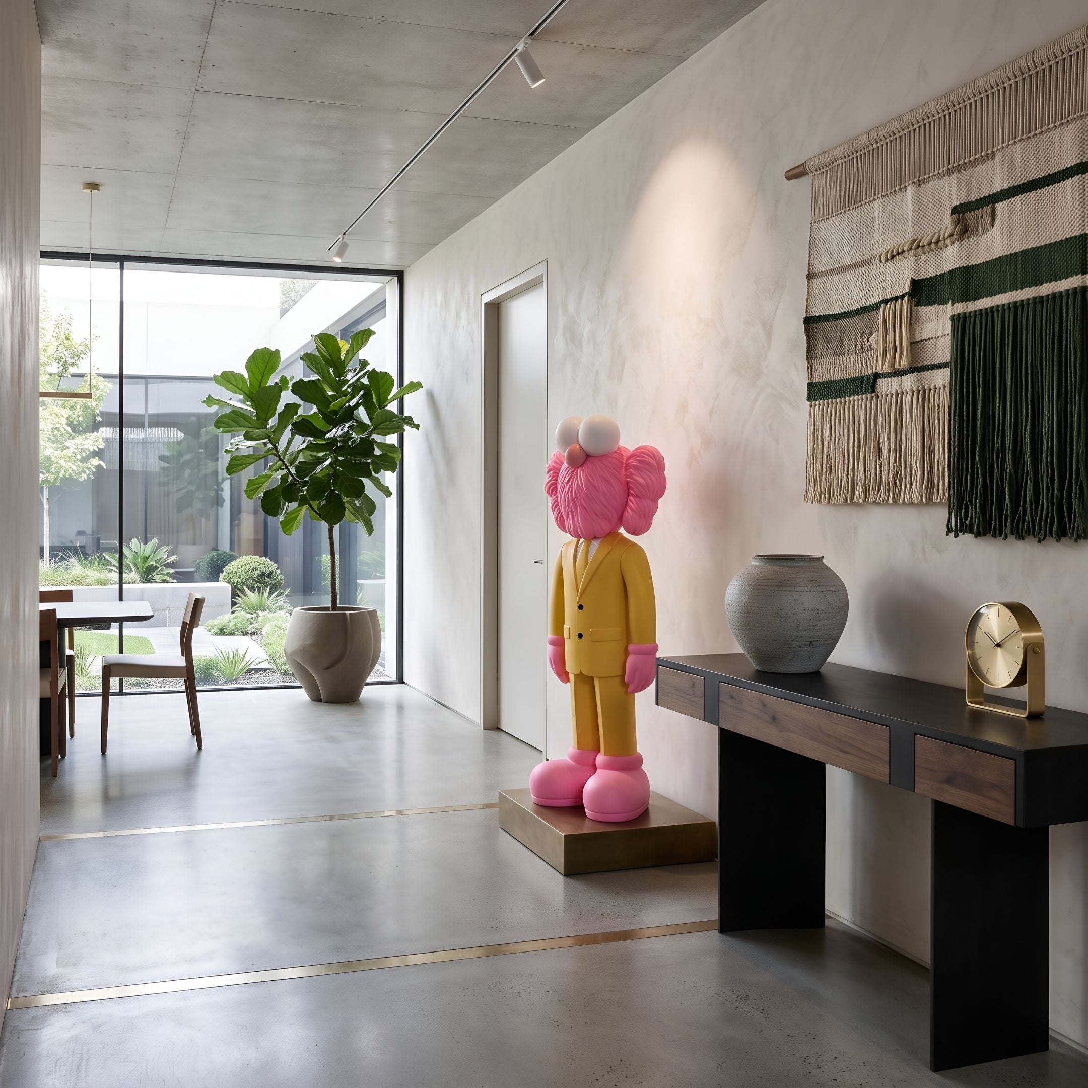 Sunbeam Yellow Suit Iconify CEO Sculpture, 130cm, yellow-suited figure with pink accents on a plinth in an entryway beside a console table and woven wall hanging.