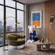 Ex-Display White & Blue Iconify Melancholy Sitting Sculpture, 130cm, seated on a black cube plinth in a living room beside an olive chair and travertine coffee table.