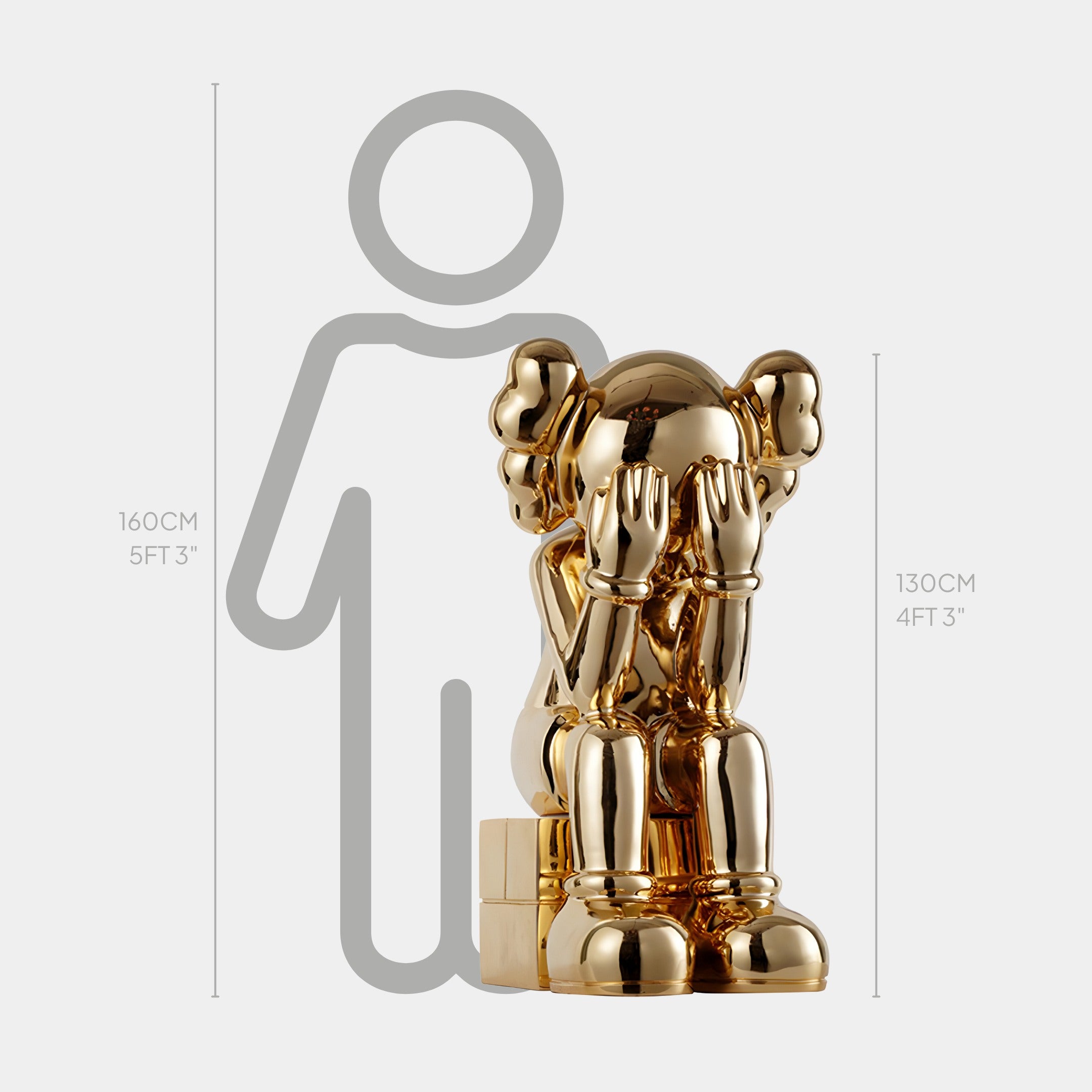 The Giant Sculptures Antique Gold Iconify Melancholy Sitting Sculpture stands at 130cm, featuring a shiny gold character with large ears in a contemplative pose. A gray silhouette highlights the 1ft height difference against a 5ft 3in person, showcasing its modern artistry.