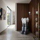 Slate Grey Iconify Melancholy Sitting Sculpture, 130cm, seated on a grey block with head in hands, displayed near a wood-paneled wall in a modern hallway.