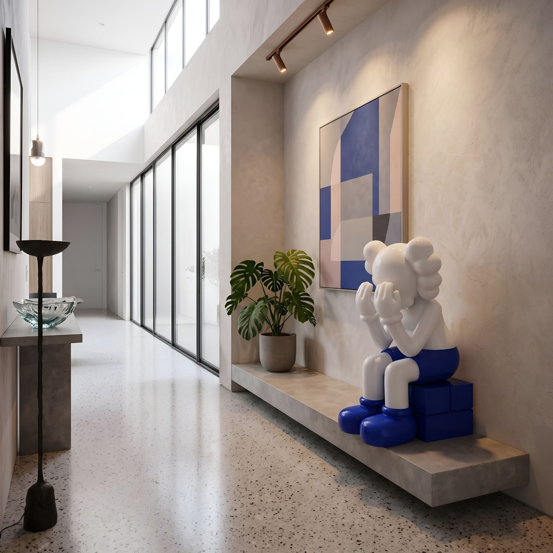 White & Blue Iconify Melancholy Sitting Sculpture, 130cm, on a hallway shelf beside a plant and framed art, resin figure with blue cube base.