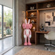 Coral Pink Iconify Rabbit Sculpture, 130cm, by Giant Sculptures, standing beside a wooden desk and shelving unit in a home office with desert views.