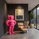 Electric Pink Iconify Rollo Warrior Sculpture, 130cm, hands-on-hips pose beside a tan leather lounge chair in a dark-walled room with framed art.