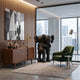 Obsidian Black Iconify Embrace Sculpture (135cm) by Giant Sculptures, two figures hugging in glossy black resin, displayed on a rug beside a green armchair and walnut sideboard.