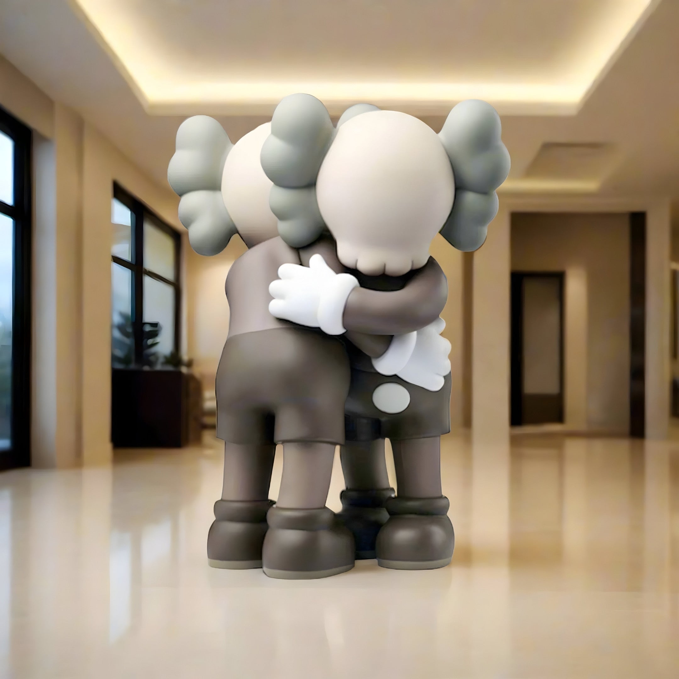 The Hazelnut Brown Iconify Embrace Sculpture - 135cm by Giant Sculptures features two cartoon-style figures with skull-like heads and gray limbs embracing in a warmly lit, modern hallway with large windows that highlight their emotional connection amidst sleek, contemporary design.