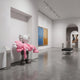 Petal Pink Iconify Rescuing Furry Sculpture, 135cm, grey figure cradling a pink companion, displayed in a gallery alcove near abstract wall art.