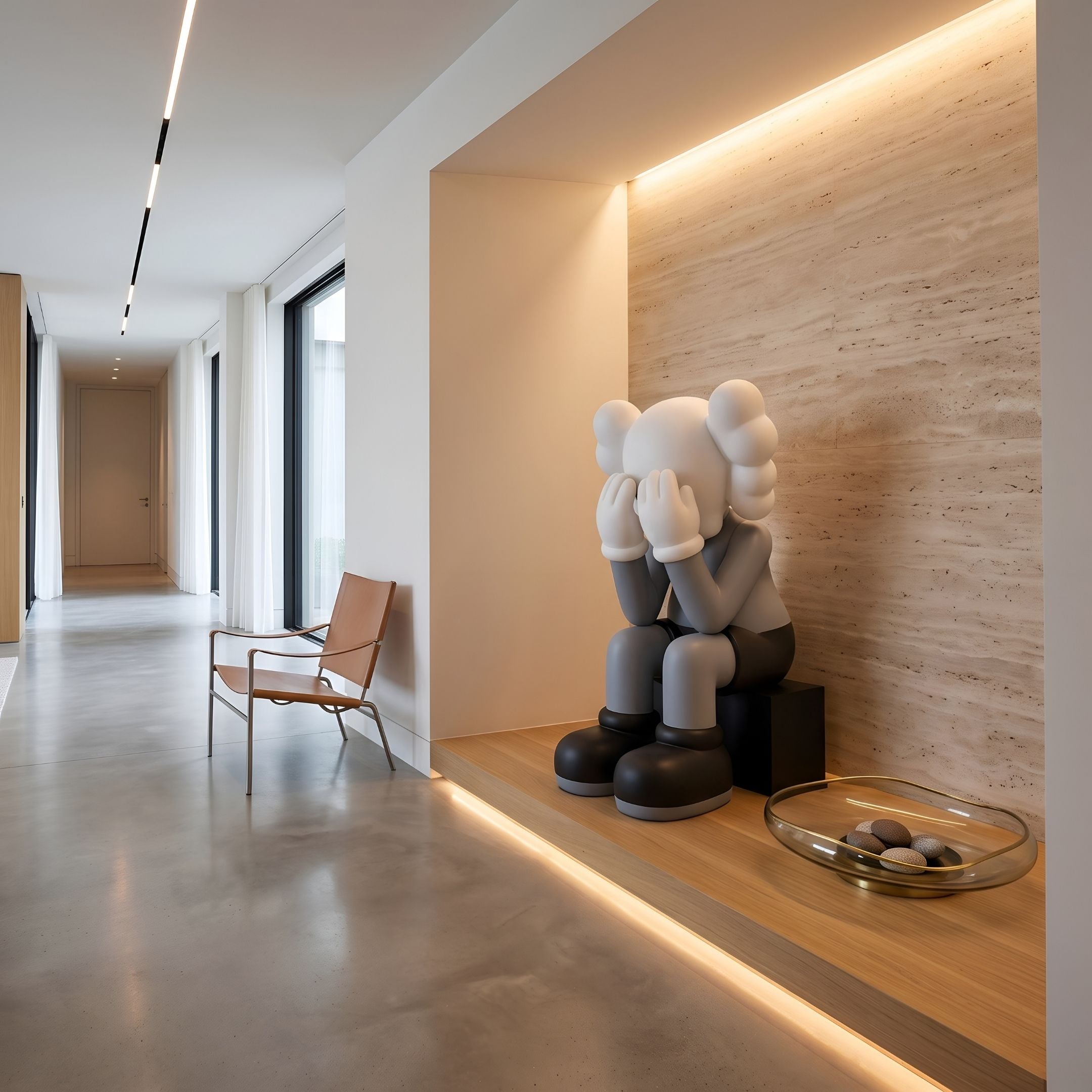 Soft Grey Iconify Sitting Sculpture, 135cm, seated figure covering its face on a wood platform in a hallway niche with travertine wall and leather chair nearby.