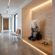 Soft Grey Iconify Sitting Sculpture, 135cm, seated figure covering its face on a wood platform in a hallway niche with travertine wall and leather chair nearby.