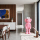 Petal Pink Iconify Furry Sculpture - 135cm displayed on a rug in a dining area with wood-paneled walls, near a table and abstract art.