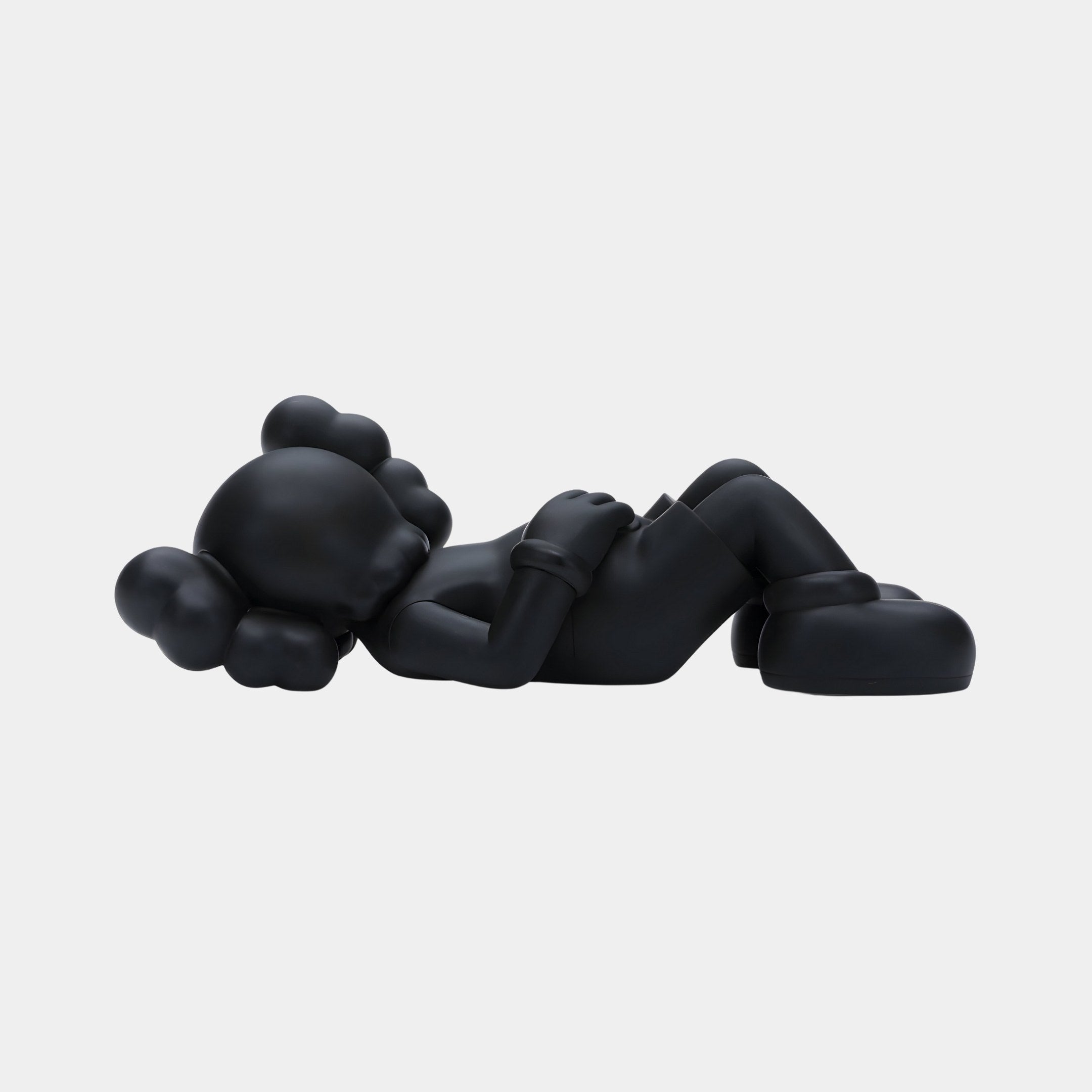 The Obsidian Black Iconify Peace Figure by Giant Sculptures is a 14cm stylized sculpture with a smooth, black cartoon-like design. It features large round ears, exaggerated limbs, and oversized shoes, lying on its back with hands on its stomach against a plain white background.