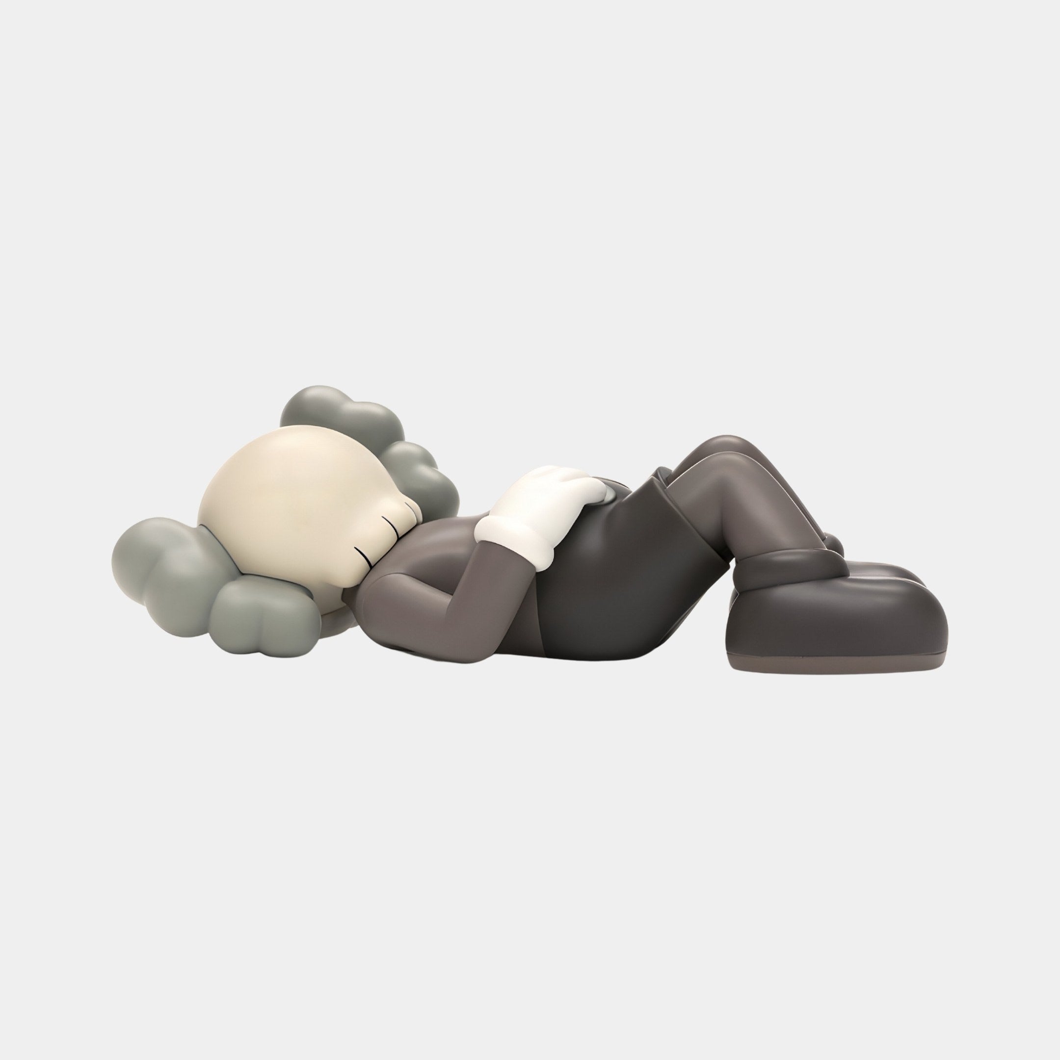 The Hazelnut Brown Iconify Peace Figure - 14cm by Giant Sculptures depicts a gray cartoon character lying on its back with arms folded, large shoes, gray hair, and closed eyes, suggesting relaxation against a plain light gray background in a minimalist décor.