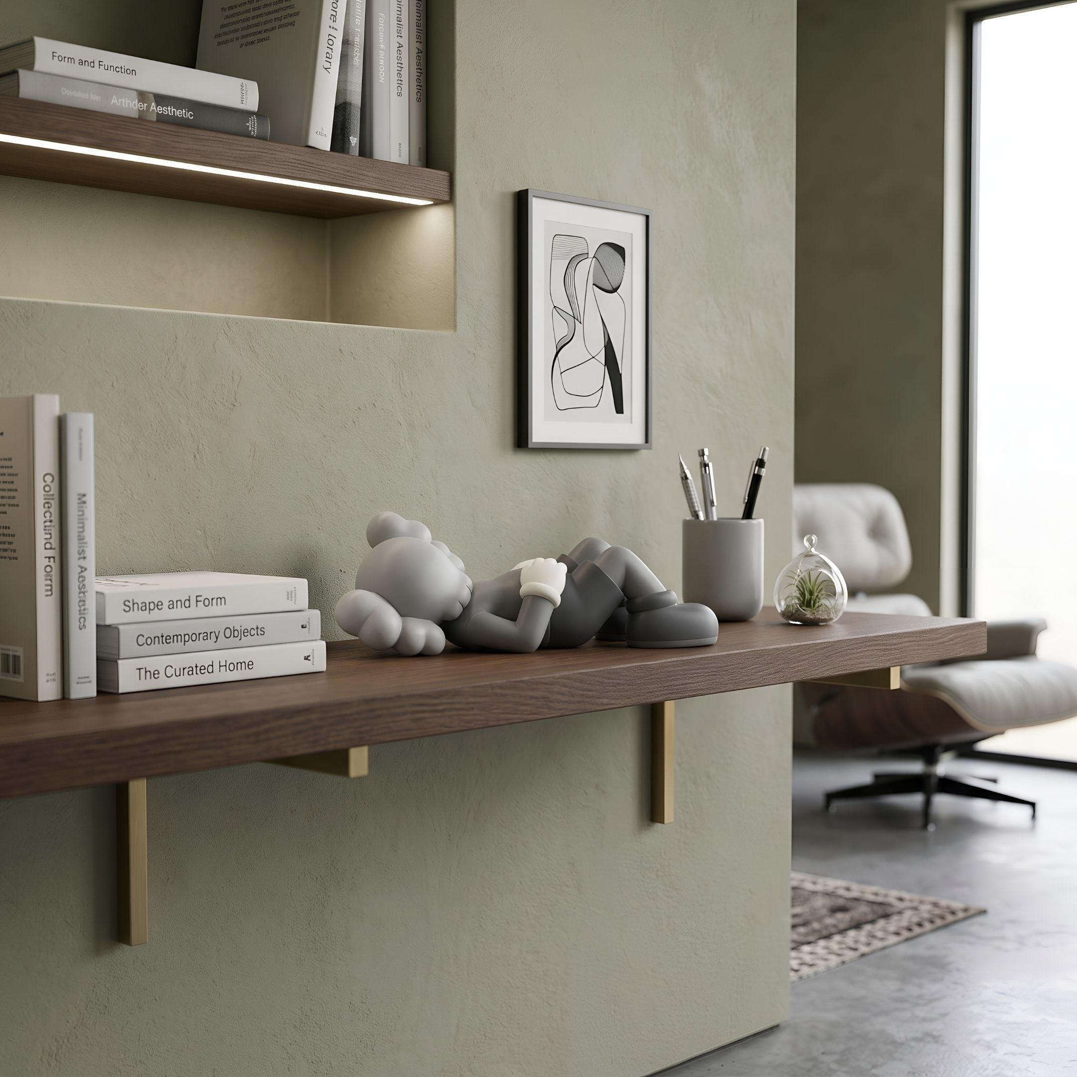 Soft Grey Iconify Peace Figure - 14cm reclining on a wood shelf beside books, a pen cup, and framed abstract art in a living room setting.