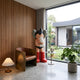 Fiery Red Iconify Cosmic Boy Sculpture, 140cm, covering face with white-gloved hand, red boots, shown by a leather chair near a sunlit window.