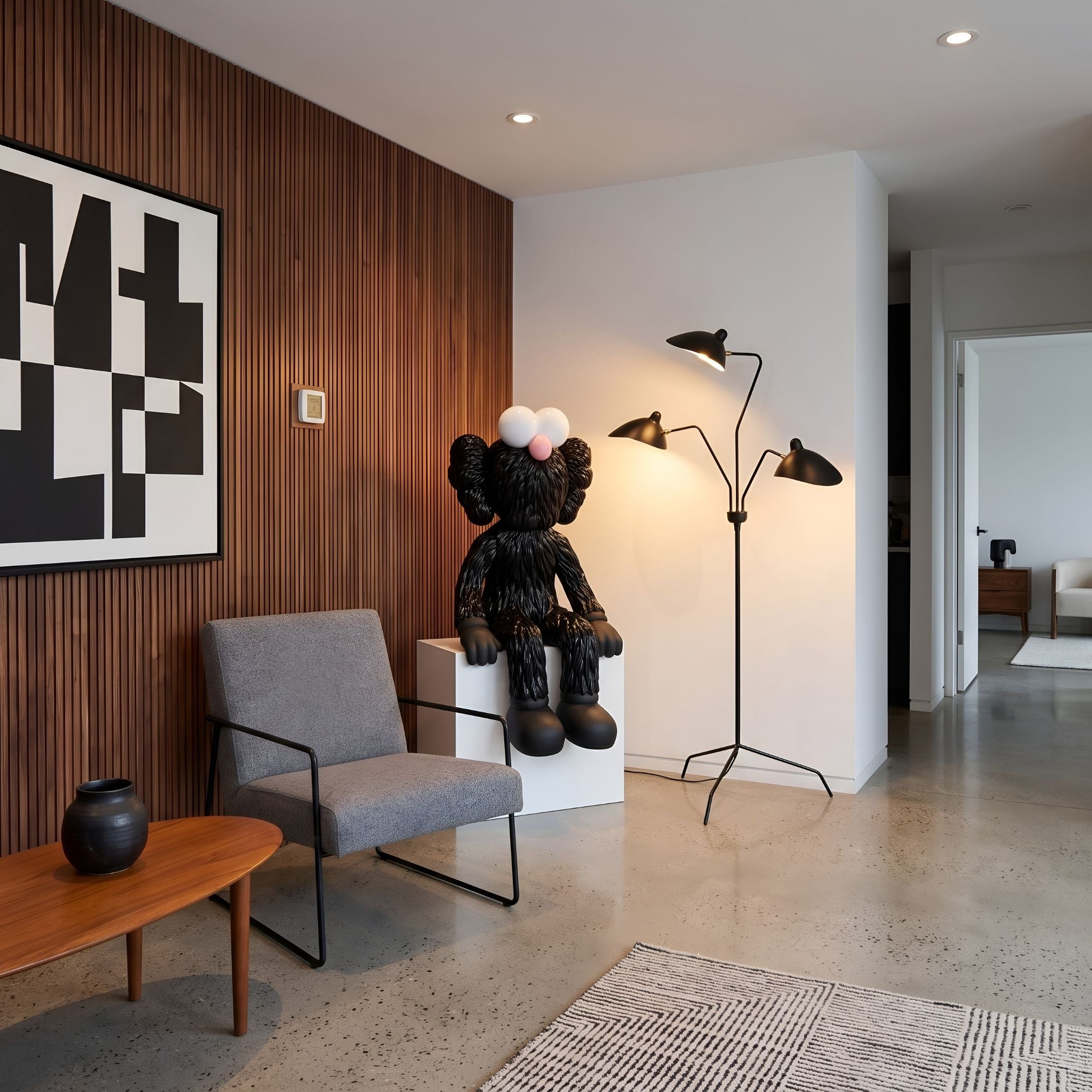 Obsidian Black Iconify Furry Sitting Sculpture, 140cm, seated on white platform in living room beside grey chair, wood-slat wall, and black tripod floor lamp.