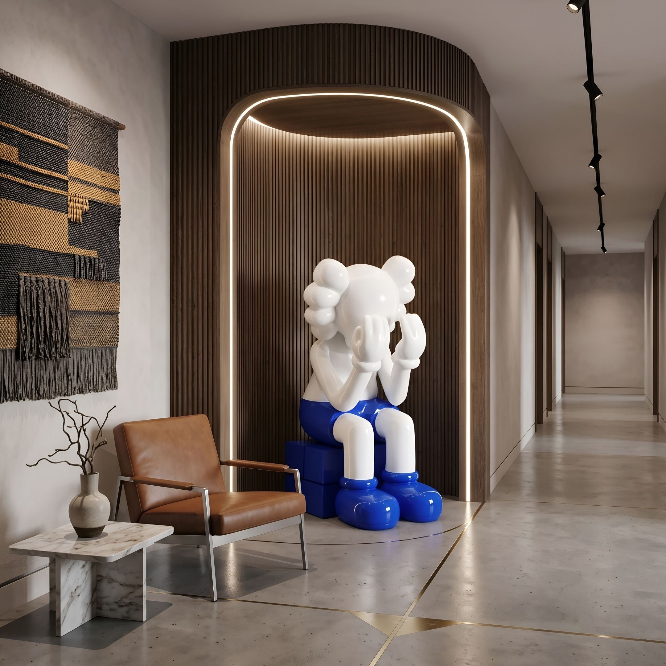 White & Blue Iconify Melancholy Sitting Sculpture, 163cm resin figure with head in hands, shown in a wood-paneled hallway niche beside a leather armchair.