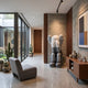 Slate Grey Iconify Melancholy Sitting Sculpture, 163cm resin figure with hands covering its face, seated on a block in a hallway beside a wooden console and cacti.