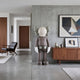 Hazelnut Brown Iconify Standing Sculpture, 168cm, resin figure with crossed-out eyes and gloved hands, shown against a concrete wall near a walnut sideboard.