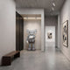 Soft Grey Iconify II Dance Sculpture - 170cm by Giant Sculptures, a grey resin figure with white gloves in a gallery hallway beside framed wall art.