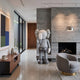 Soft Grey Iconify V Dance Sculpture, 170cm, standing in a modern living room beside a stone fireplace, walnut console, and grey armchair.