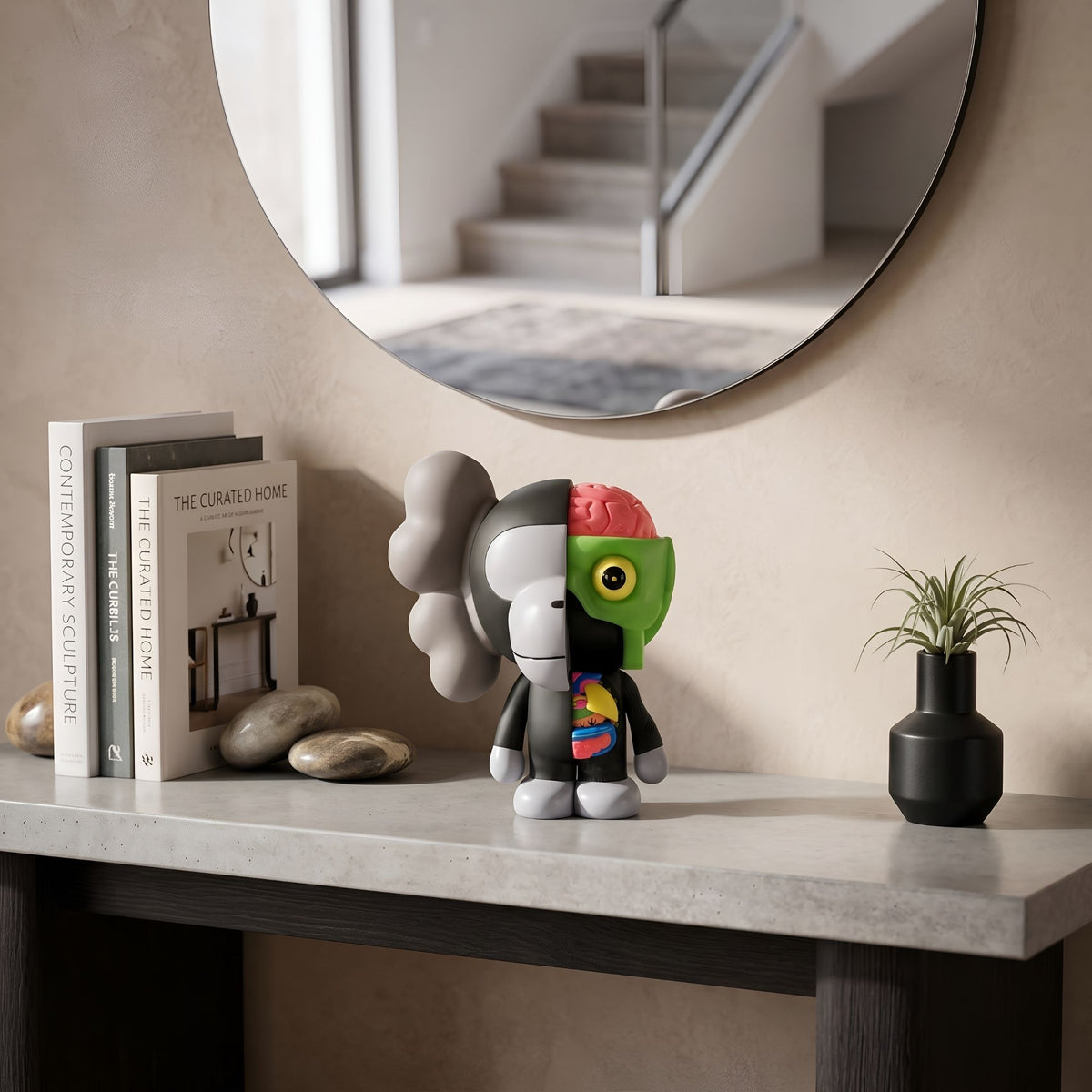Slate Grey Iconify Monkey Figure (18cm) on a console table, dual-faced design with grey skull-like side and green anatomical side, styled near books, stones, and a mirror.