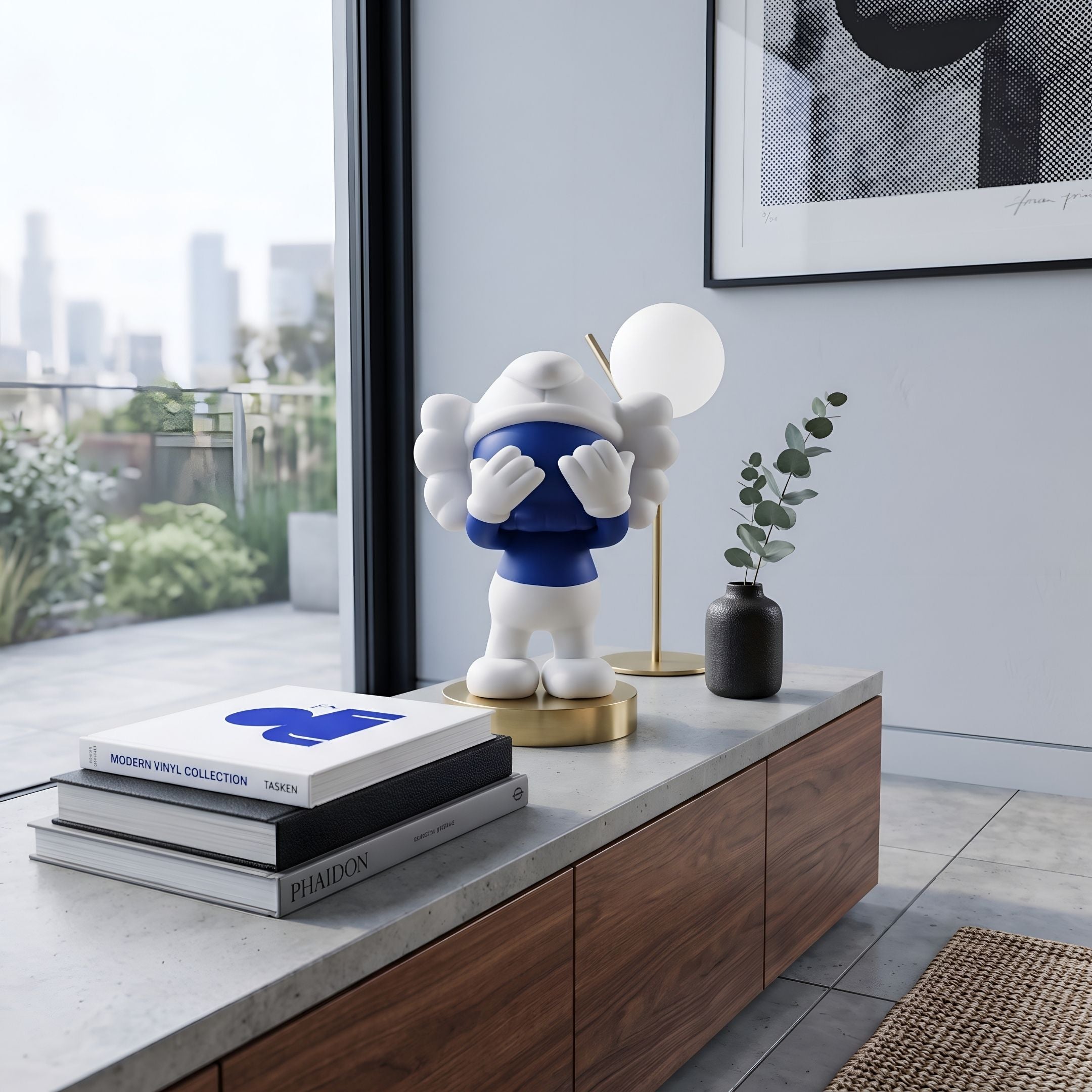 Deep Blue Iconify Peekaboo Figure, 20cm, covering its face with white hands on a wooden console beside books, a globe lamp, and framed art.