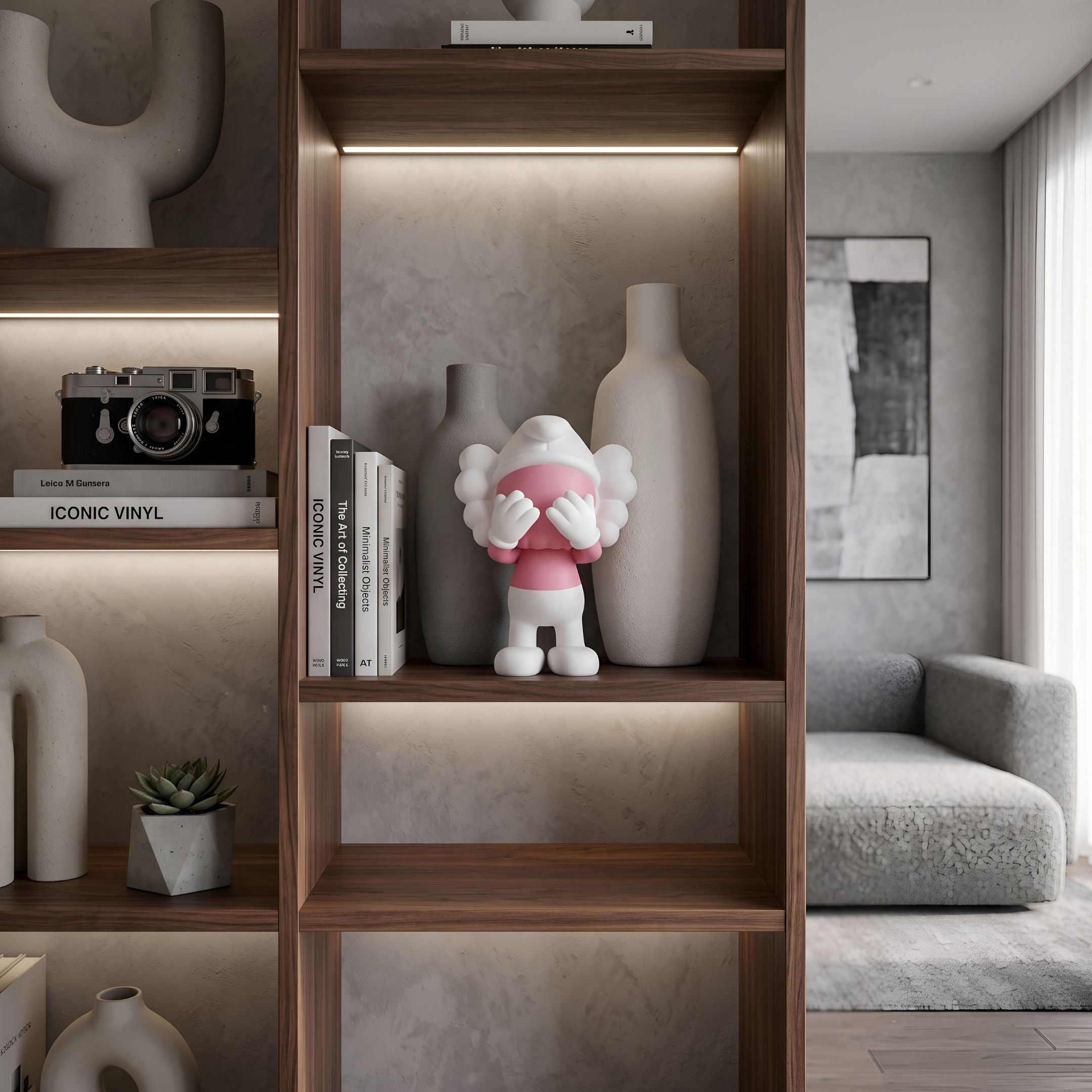 Petal Pink Iconify Peekaboo Figure - 20cm displayed on a wooden shelf beside vases and books, in a living room with a grey sofa.