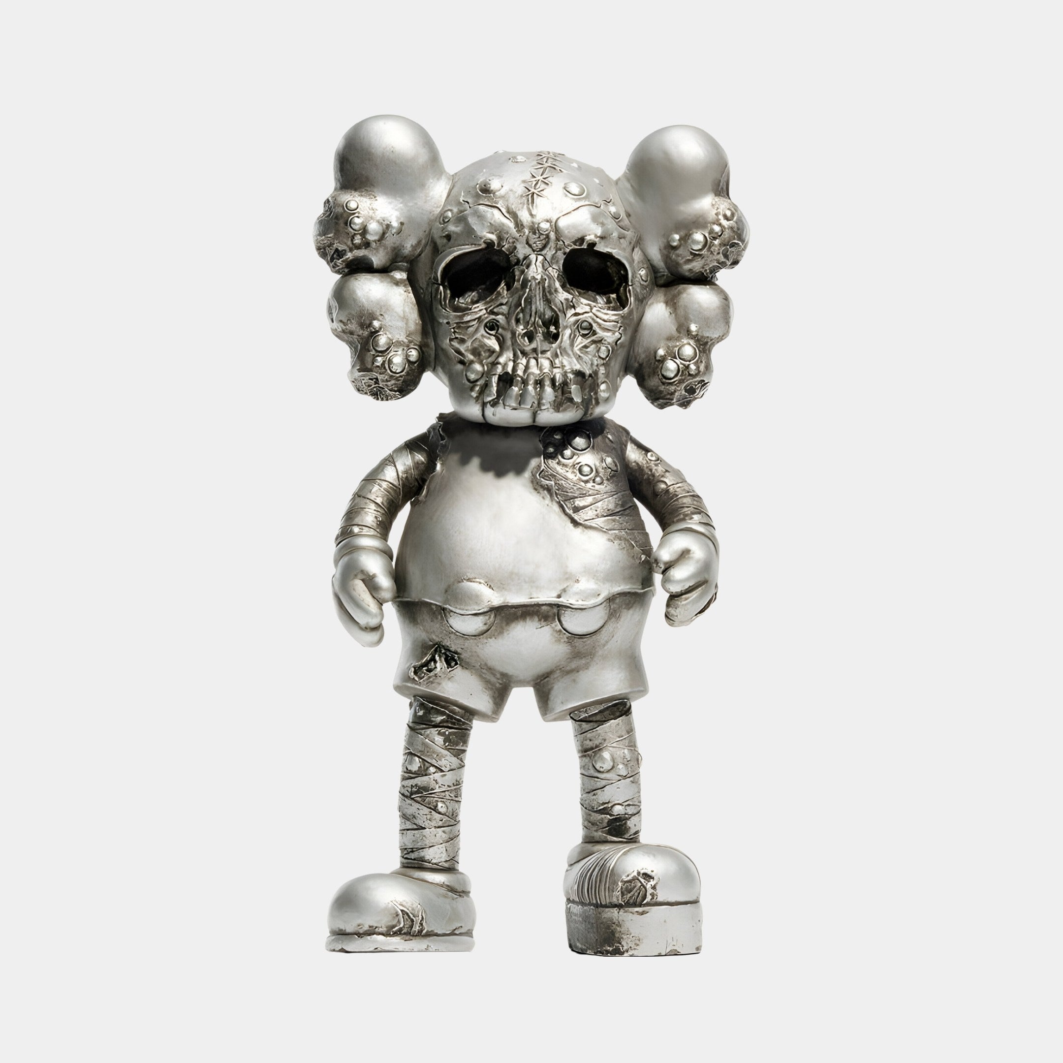 The Weathered Silver Iconify Scar Figure - 20cm by Giant Sculptures is a metallic figurine with a large skull-like head and bulbous ears, blending robotic and organic textures in silver. It features shorts and shoes against a simple background.