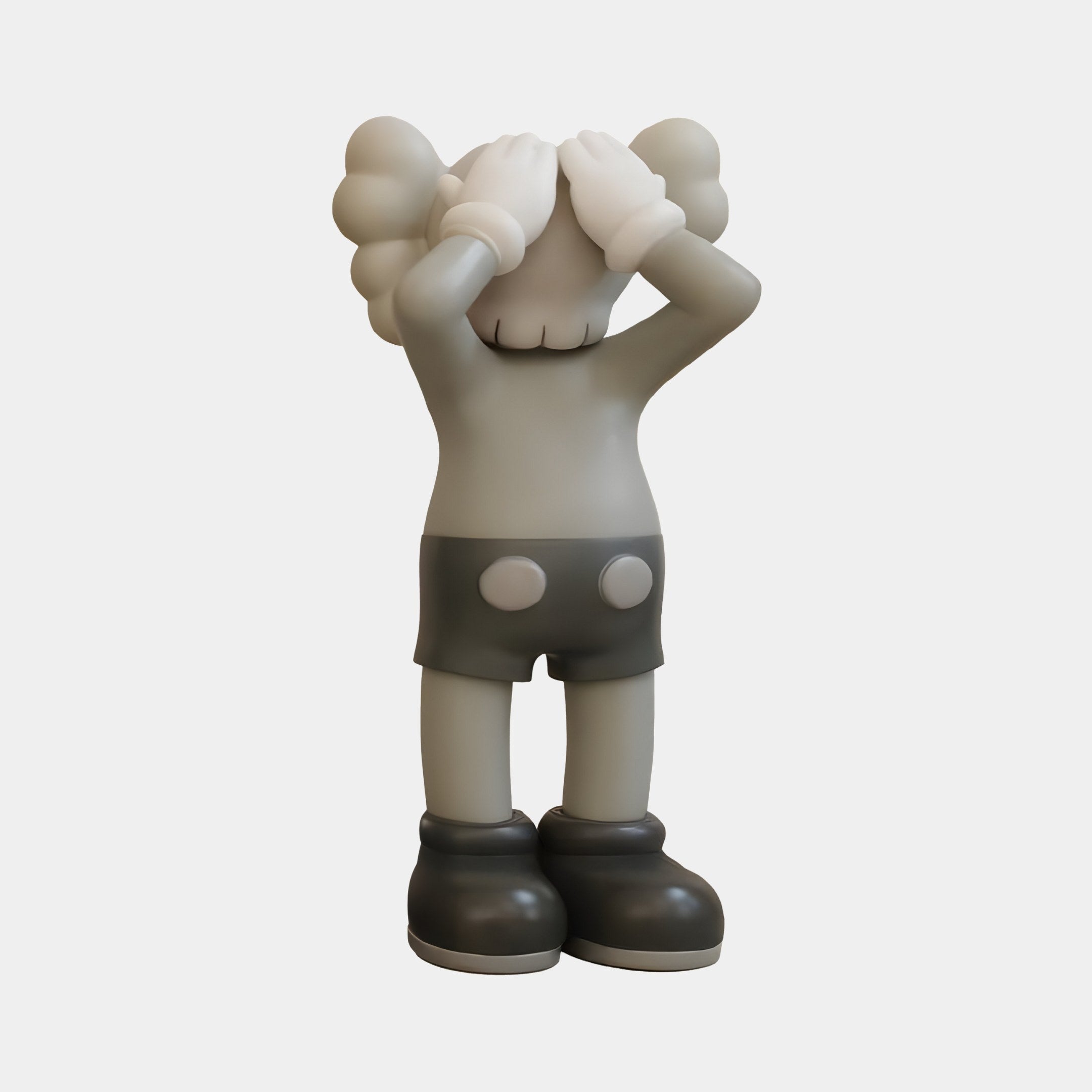 The Soft Grey Iconify Silent Cry Figure by Giant Sculptures features a minimalist, cartoonish design with gloved hands over its eyes, rounded shapes on its head, shorts with two dots, and large shoes. Made to stand out quietly against a plain white background.