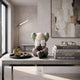 Hazelnut Brown Iconify Sorrow Figure, 20cm, seated with hands covering its face, on a coffee table beside books, glasses, and a clock in a modern living room.
