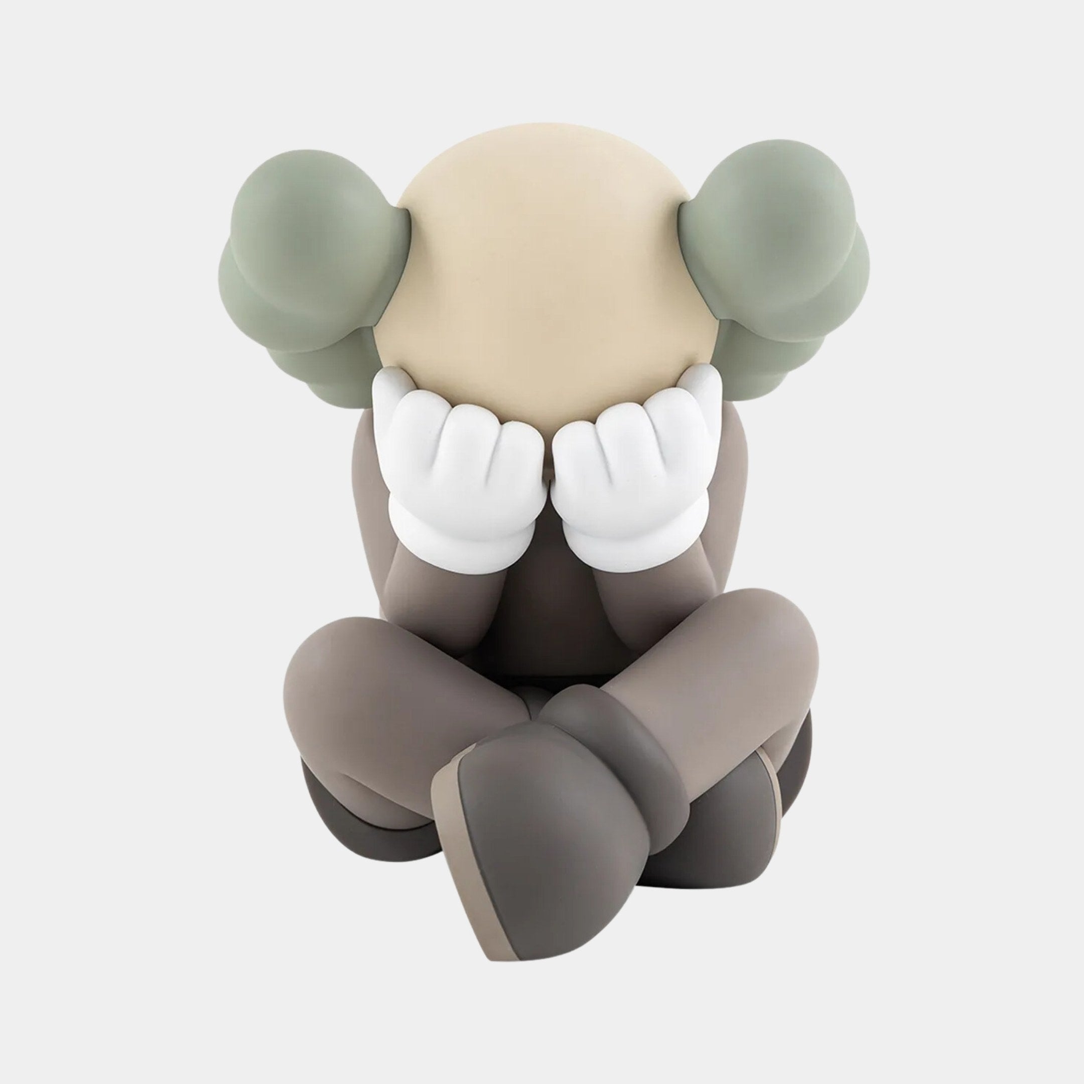 The Hazelnut Brown Iconify Sorrow Figure by Giant Sculptures is a 20cm seated sculpture, featuring a round beige head with crossed legs, hands covering its face, green ear-like appendages, large white gloves, and dressed in earthy tones.