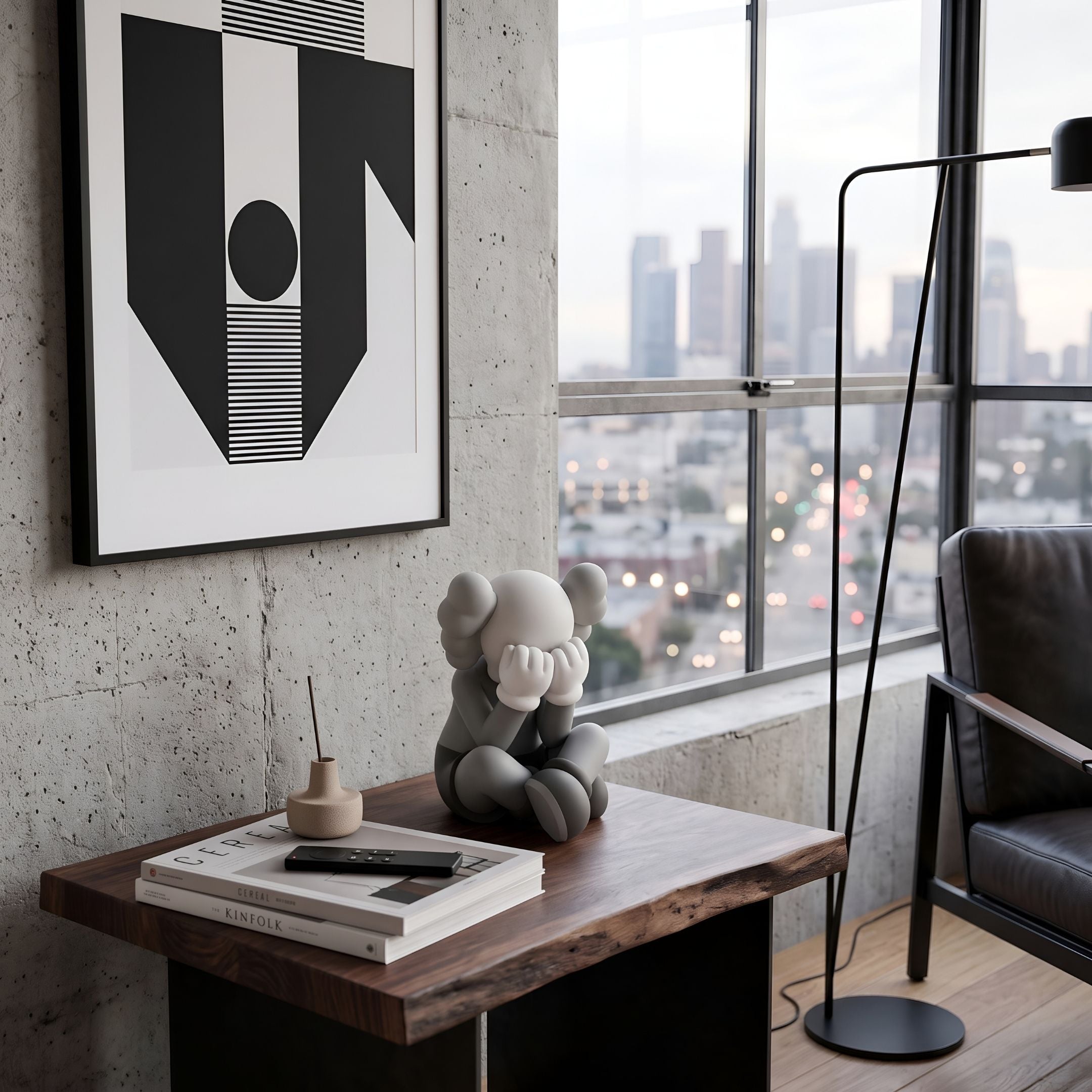 Soft Grey Iconify Sorrow Figure (20cm) seated with hands covering face on a wooden side table, styled near books and a city-view window.