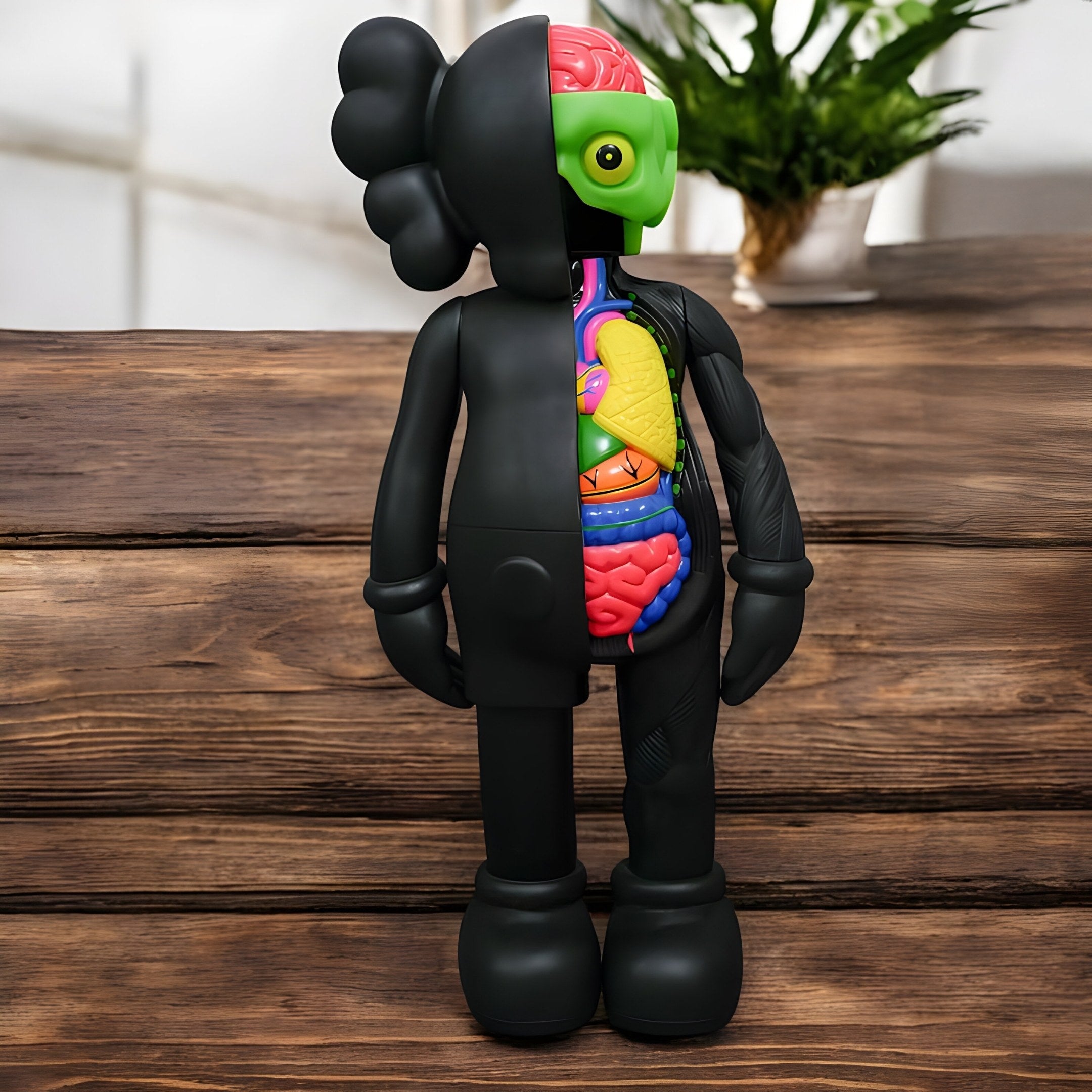 The Giant Sculptures Midnight Black Iconify Anatomy Figure (20cm) features a sleek black exterior with exposed, colorful anatomy. It stands on wood, accented by a blurred plant in the background, adding to its modern mystique.