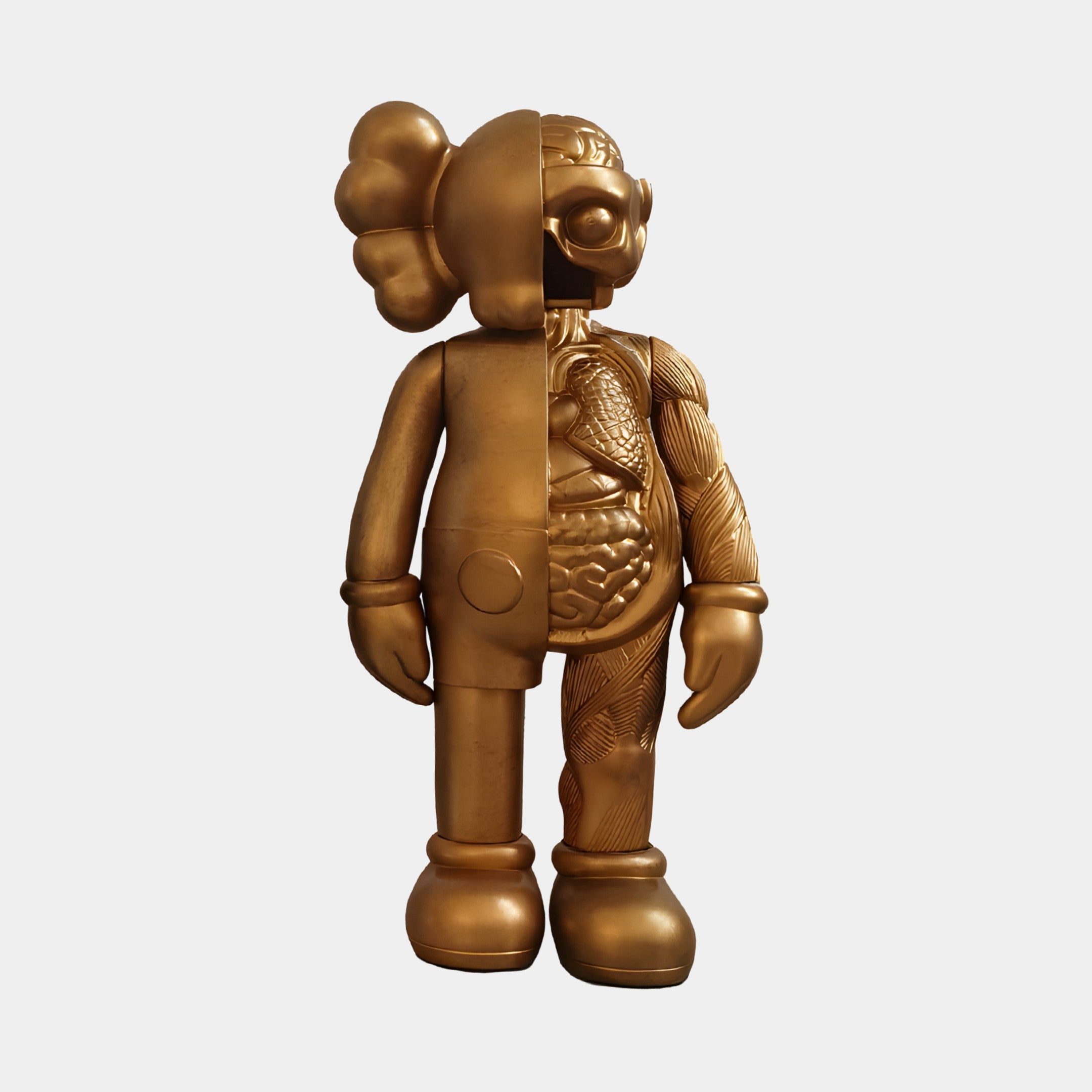 The Antique Brushed Gold Iconify Anatomy Figure - 20cm by Giant Sculptures has a split design: one side is smooth and cartoonish with a round head and big shoes, while the other side displays a detailed anatomical interior. Made from resin, it blends whimsy with intricate detail.