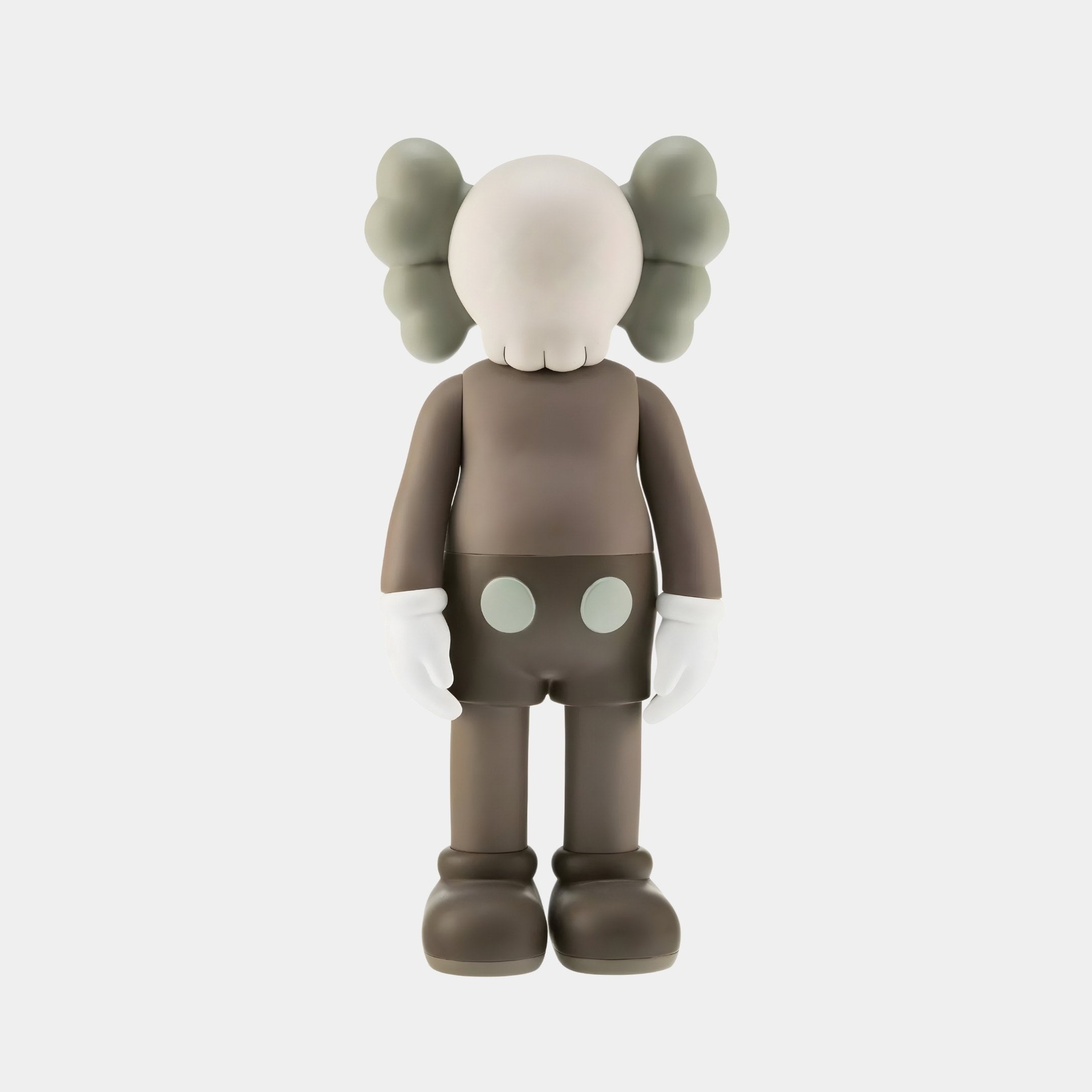 The Hazelnut Brown Iconify Standing Figure by Giant Sculptures is a 20cm resin sculpture. It has a round head, large ears, and faceless expression, with a gray body, white glove-like hands, and shorts with two dots. Its minimalistic design adds elegance to any cozy setting with muted colors.