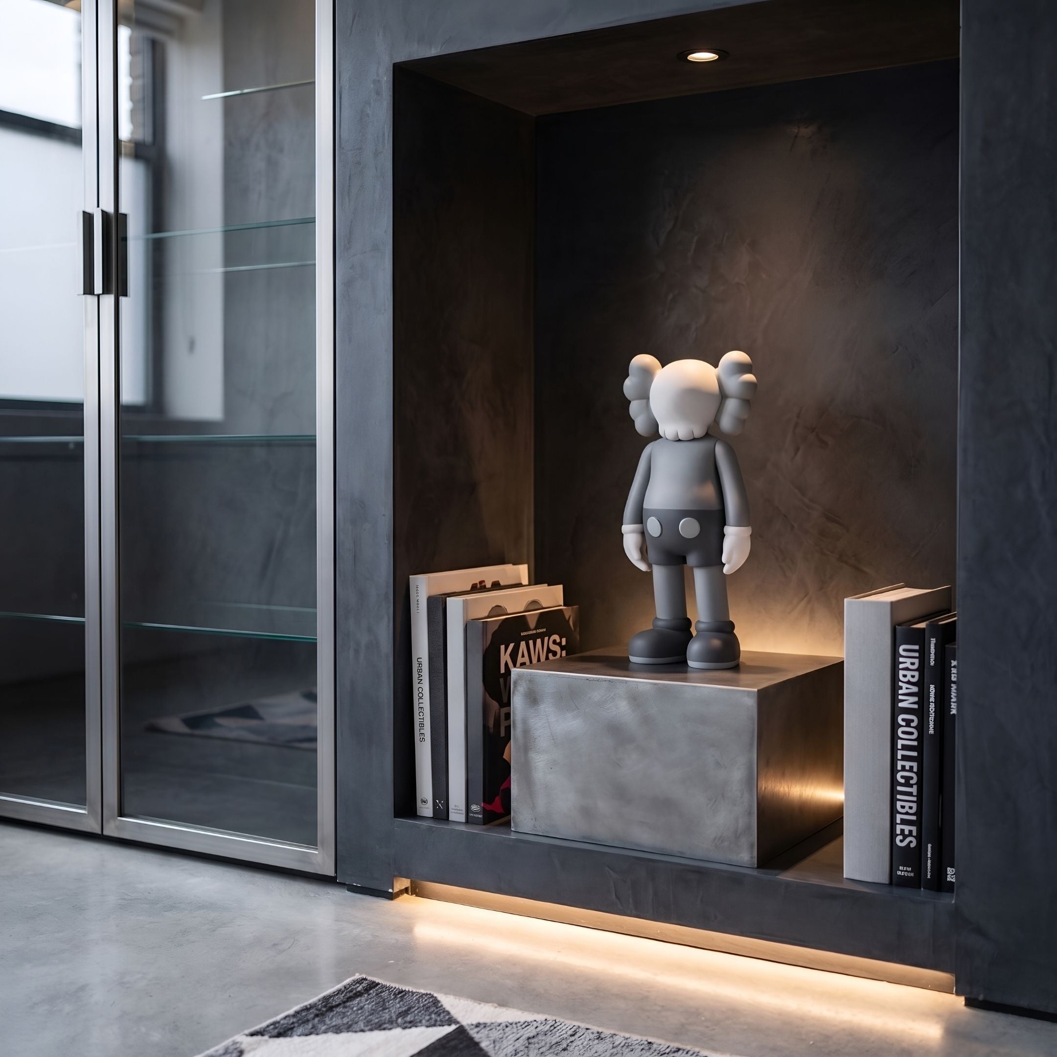 Soft Grey Iconify Standing Figure - 20cm displayed on a concrete pedestal in a dark built-in niche with books and warm accent lighting.