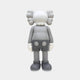 The Soft Grey Iconify Standing Figure by Giant Sculptures is a 20cm tall piece with a round head, X-shaped eyes, large ears, and dressed in gloves, shorts, and boots. This minimalist cartoon character elegantly faces away on a plain background.