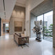 Soft Grey Iconify Family Sculpture, 200cm, in a modern lounge with sofa and abstract wall art, grey resin figure holding two smaller figures near a glass wall.