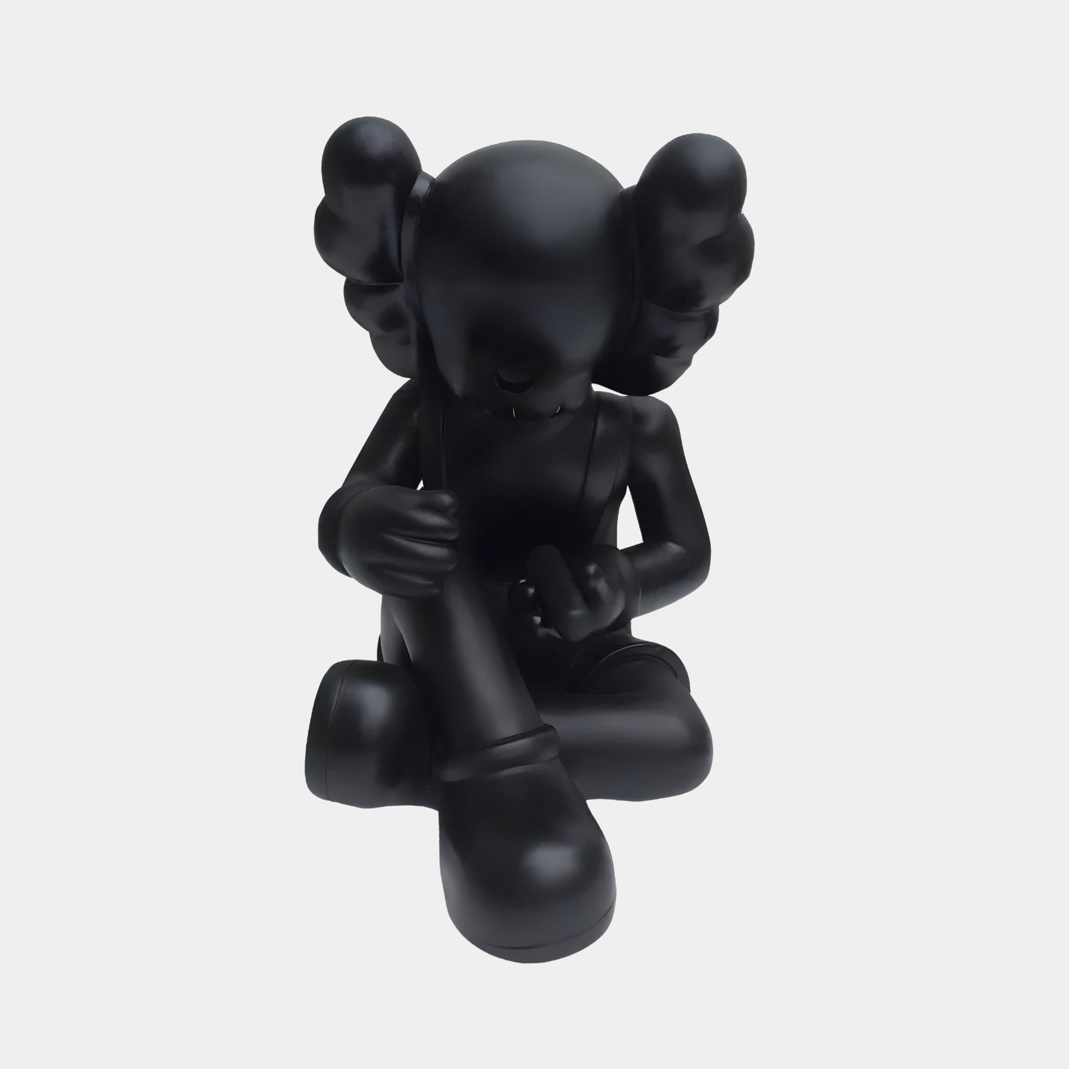 The Obsidian Black Iconify Hollow Figure - 23cm by Giant Sculptures features a cartoon-like character with crossed legs, gloved hands, and large shoes. Its hollow design and featureless face blend modern sophistication with whimsy for a playful yet somber look.