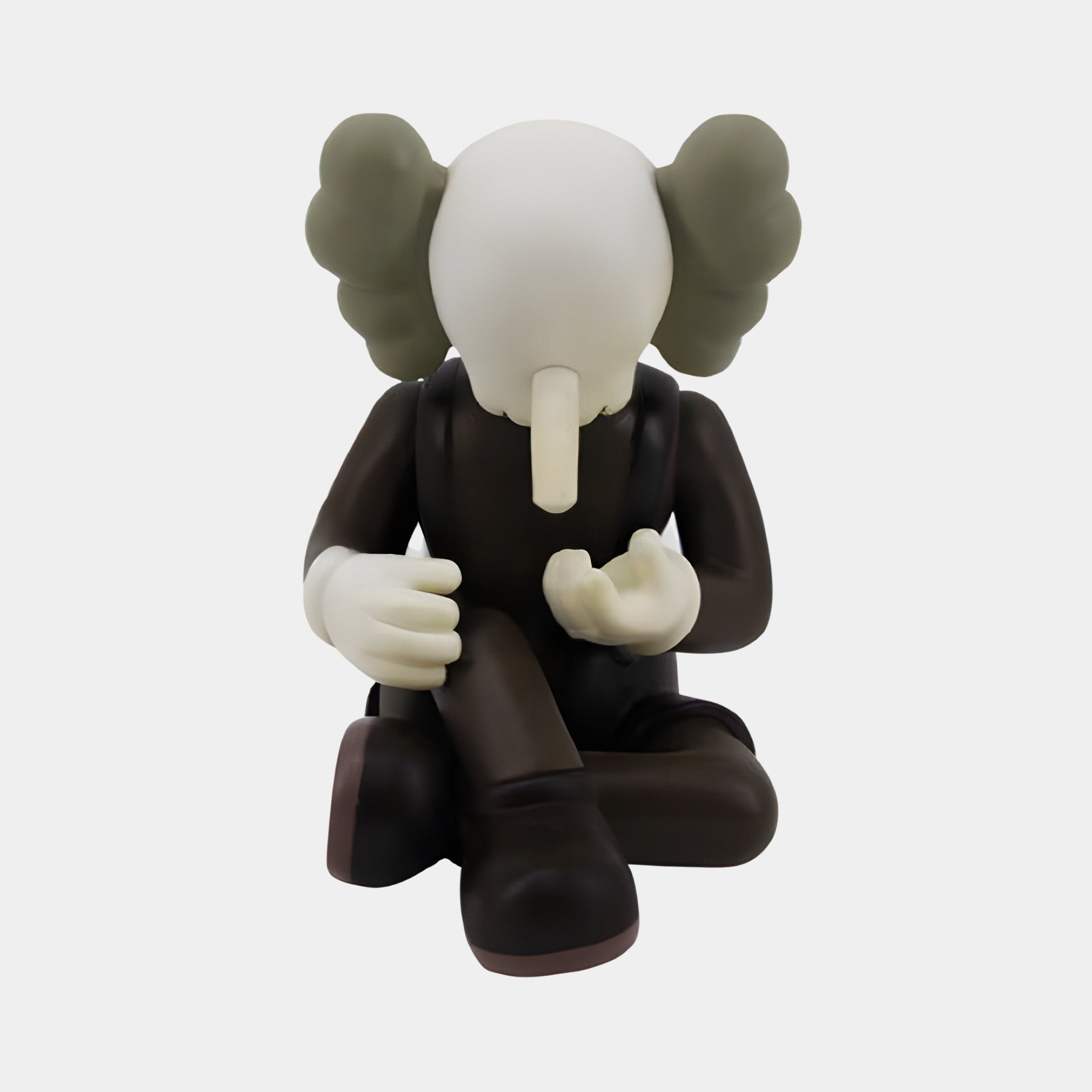 A seated cartoon figure with an elephant trunk and large ears, outfitted in dark attire and premium polyvinyl boots, conveying a contemplative or sad mood with its downcast head and clasped hands, resembles the 23cm Hazelnut Brown Iconify Hollow Figure by Giant Sculptures.