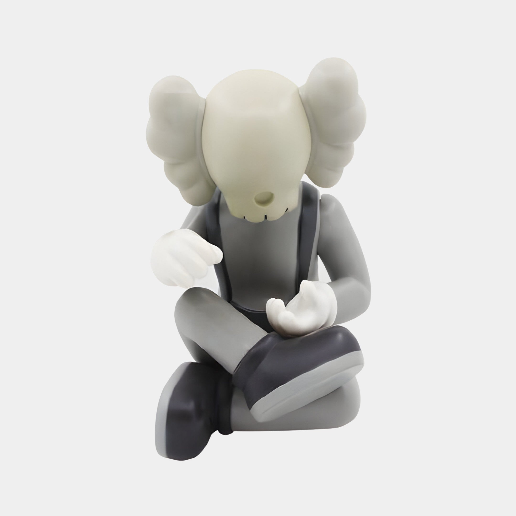 The Soft Grey Iconify Hollow Figure - 23cm by Giant Sculptures is a minimalist artistic piece featuring a skull-like head and crossed bones for ears. Its Scandinavian-inspired gray body, white gloves, and black shoes capture attention as it sits cross-legged, bent forward with expressive hand gestures.