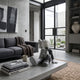 Slate Grey Iconify Anatomy Figure - 23cm seated on a concrete coffee table beside books and a mug, with a dark sofa and glass doors in a modern living room.