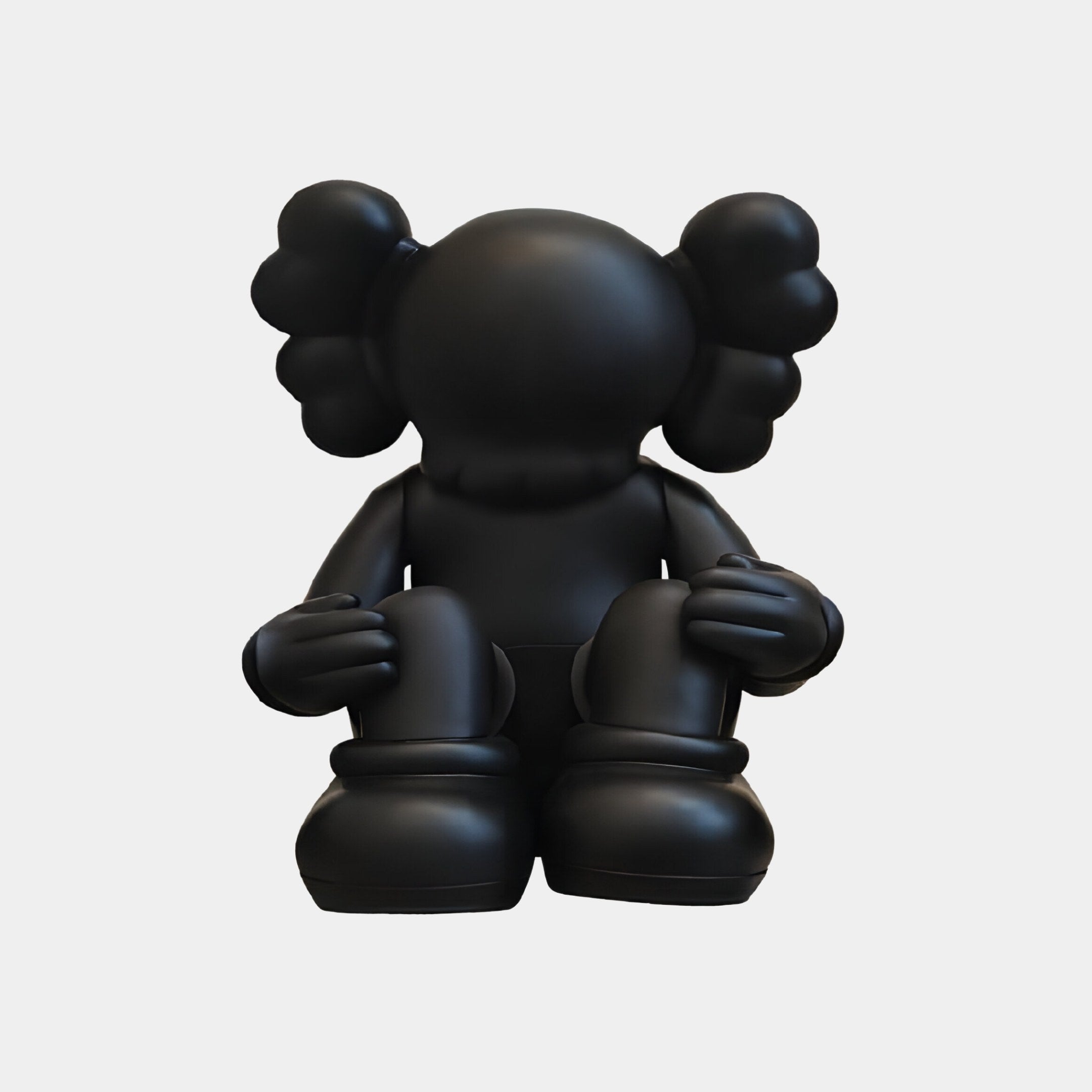 An Obsidian Black Iconify Silent Figure by Giant Sculptures, 25cm tall, crafted in a monochrome palette with large round ears and a featureless face, sits cartoon-like on the ground. Made from resin, it is set against a plain white background.