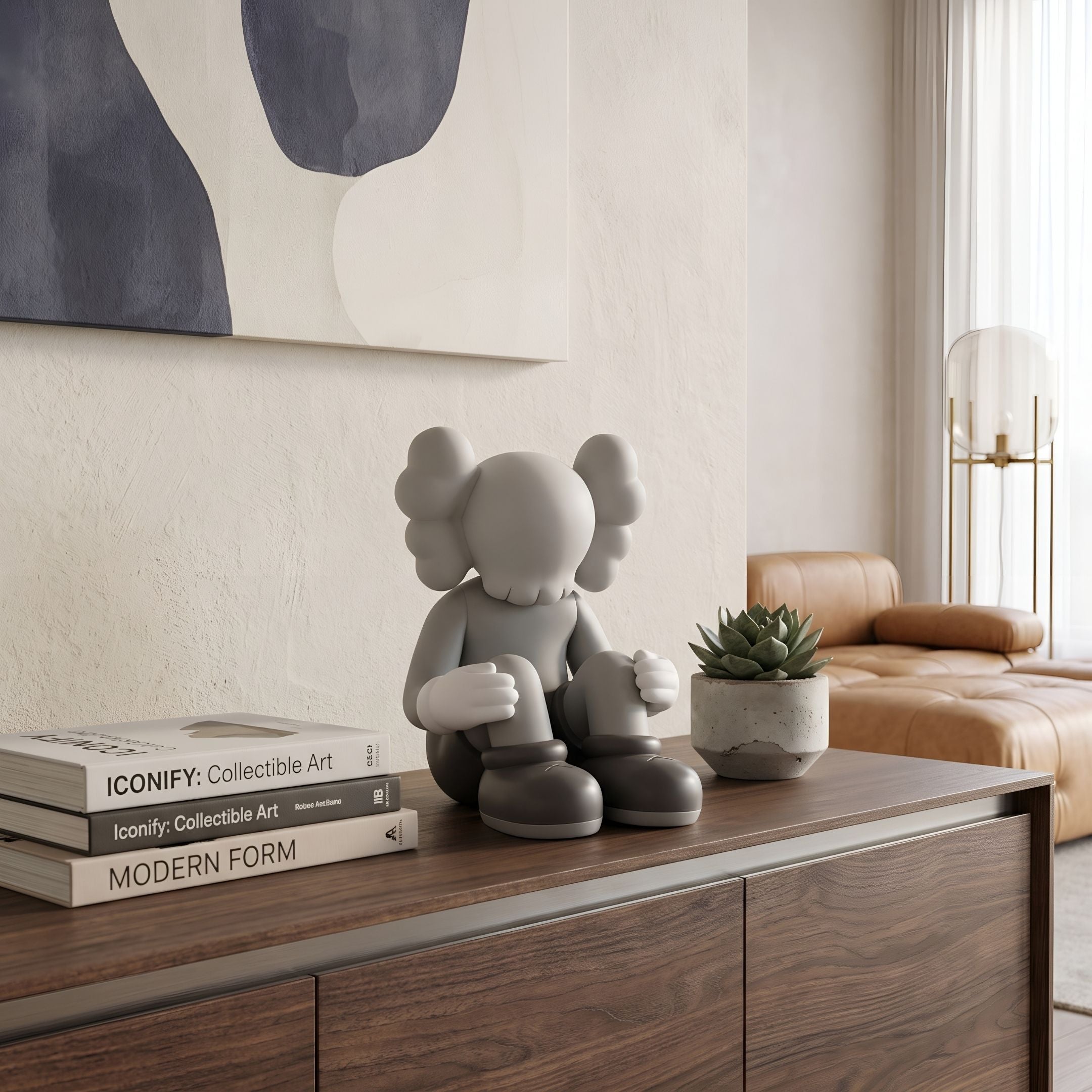 Soft Grey Iconify Silent Figure - 25cm polyvinyl sculpture seated on a wooden sideboard beside books and a succulent, with tan sofa in background.