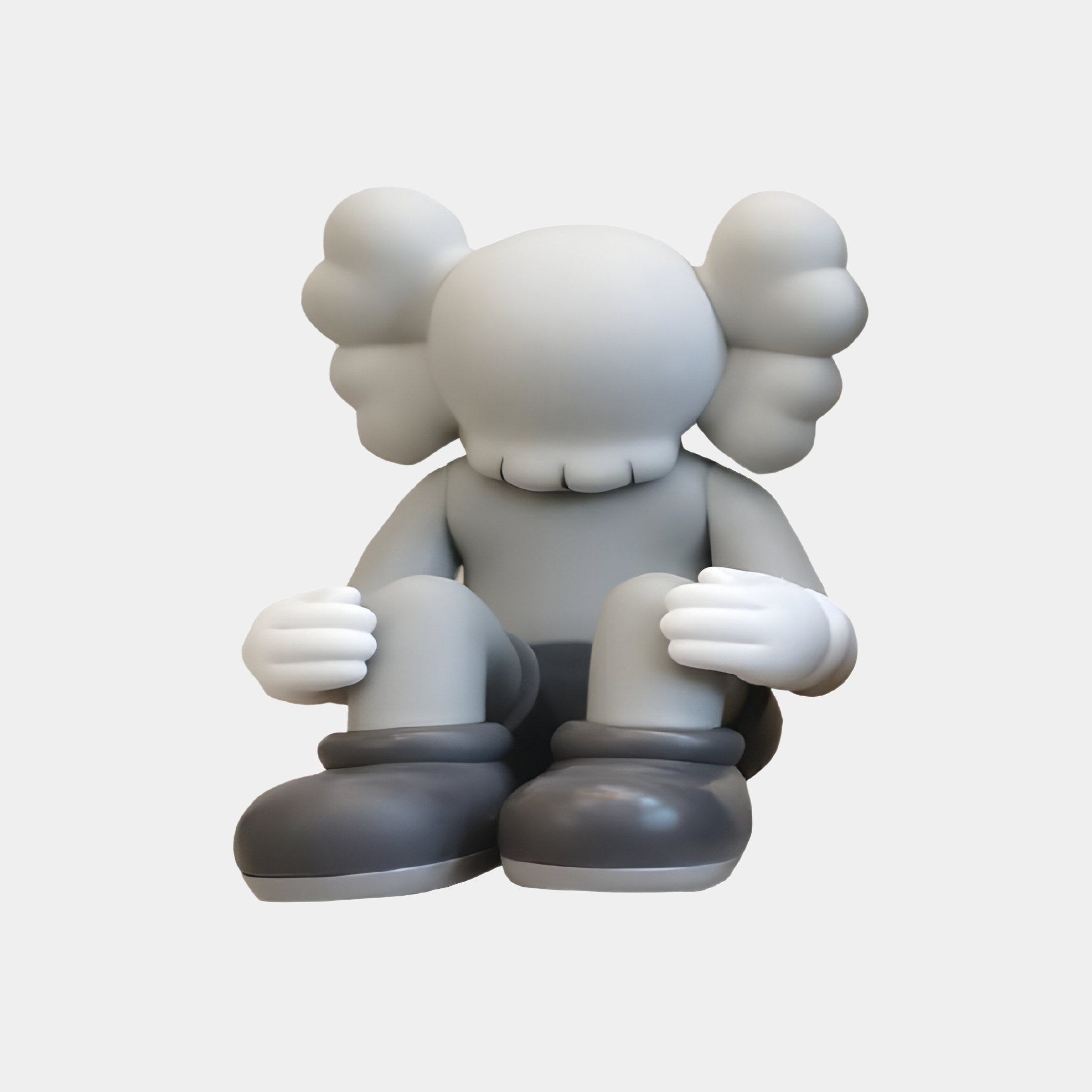 The Soft Grey Iconify Silent Figure by Giant Sculptures is a 25cm resin sculpture featuring a cartoon-like character with a smooth face, cloud-like ears, and large gloved hands. Sitting in hefty boots against a plain gray backdrop, it embodies mindfulness décor for serene spaces.