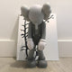 In a minimalist décor, the Soft Grey Iconify Burden Figure by Giant Sculptures—a 28cm contemporary piece with large ears and a long nose—stands slouched and sad before a canvas of black branches on white.