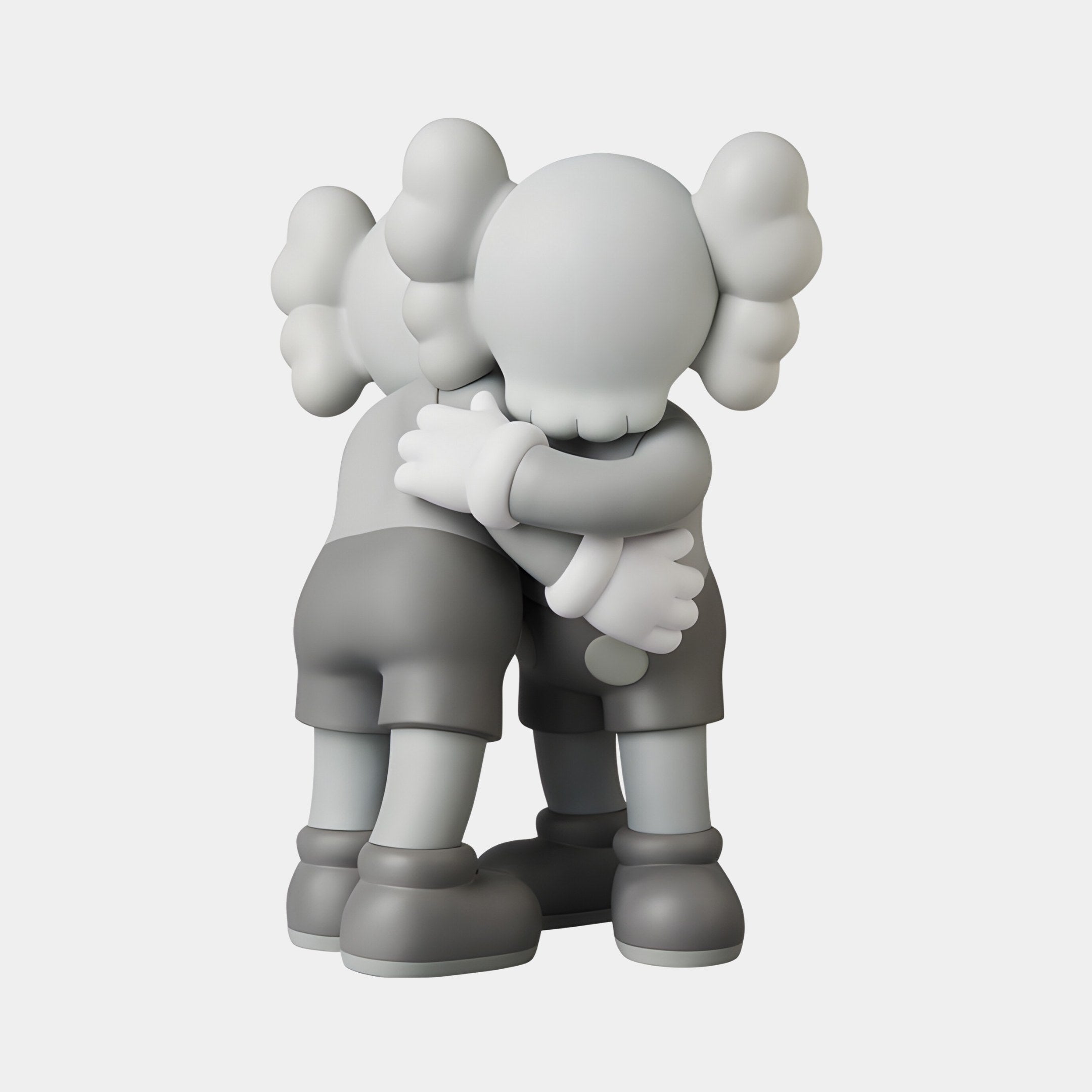 The Soft Grey Iconify Embrace Figure by Giant Sculptures features two cartoon-like figures with X-shaped eyes and unique ears in a close embrace. This 28cm resin-crafted grayscale sculpture shows them in shorts and shoes against a plain white background.